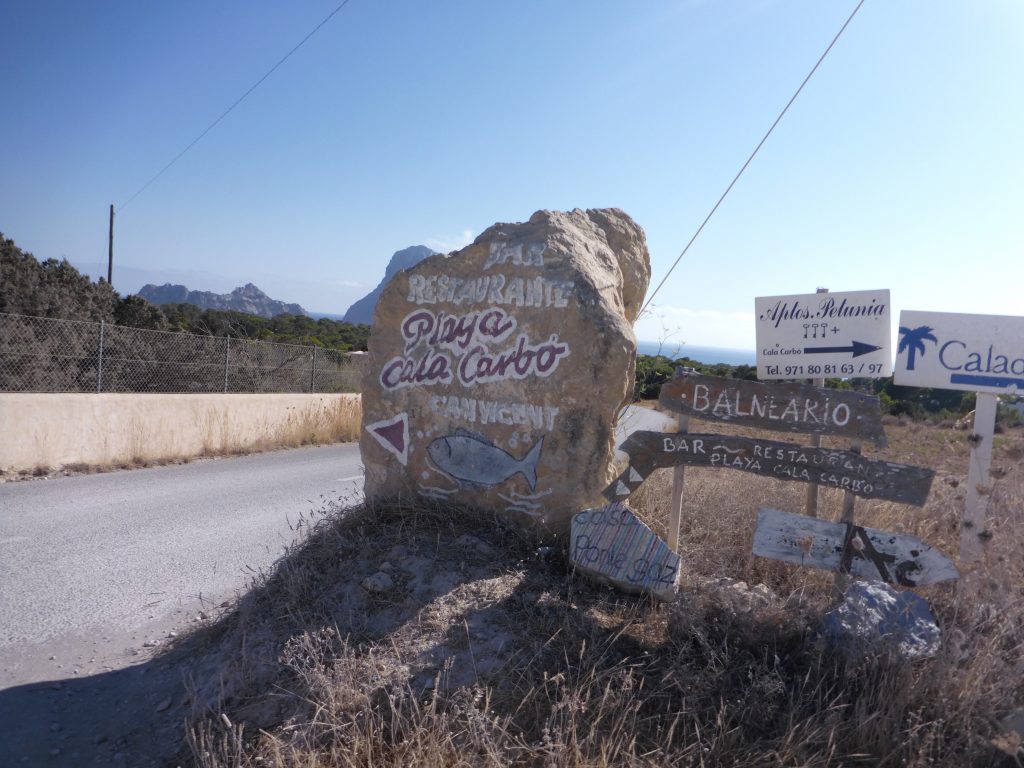 Einer der typischen Wegweiser Steine auf Ibiza. Hier Wegweiser zum Restaurant an der Playa Cala Carbo